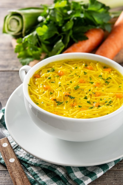 Chicken noodle soup in white bowl on wooden table