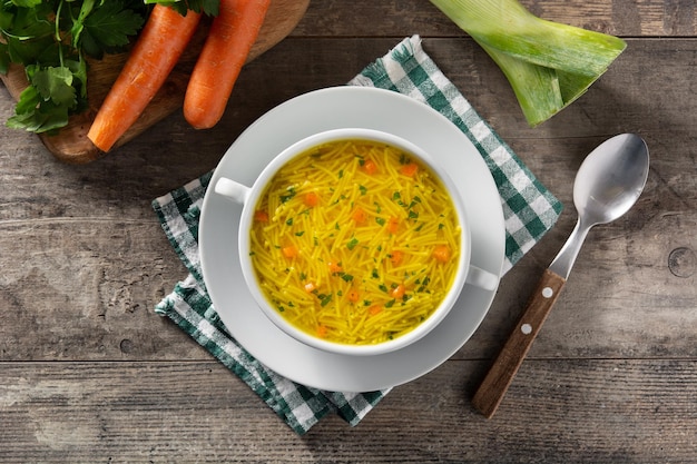 Chicken noodle soup in white bowl on wooden table