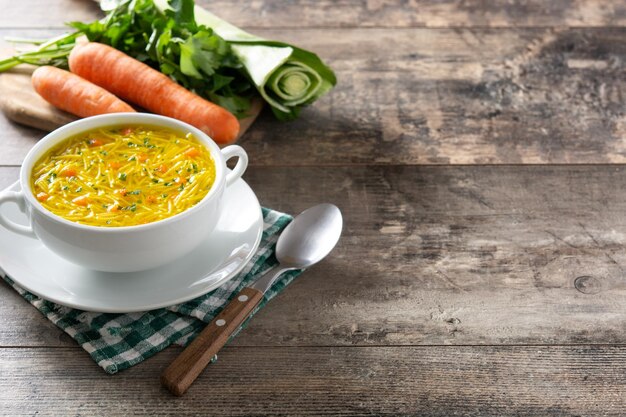 Chicken noodle soup in white bowl on wooden table