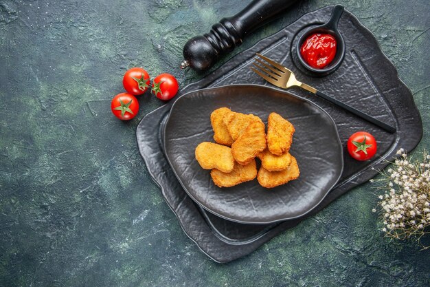 Куриные наггетсы на черной тарелке и элегантный кетчуп вилкой на темном подносе белые цветочные помидоры