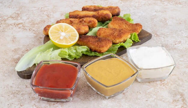 Chicken nuggets and fried sausages on a green lettuce leaf on a wooden board.