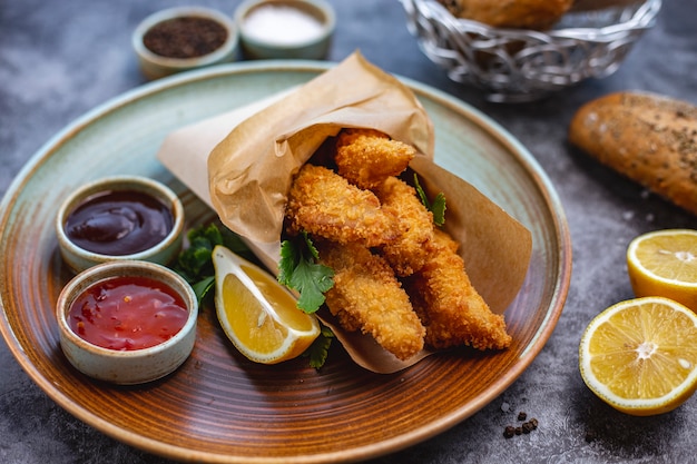 Free photo chicken nuggets in small paper bag served with lemon parsley sweet chili and bbq sauce