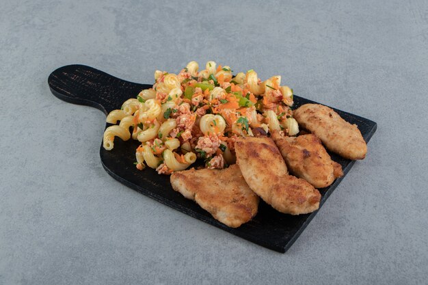 Chicken nuggets and spiced pasta on wooden board.