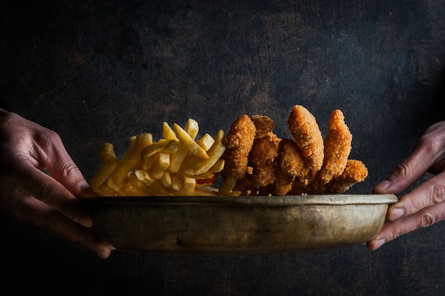 chicken nuggets with french fries and human hand in clay dishes