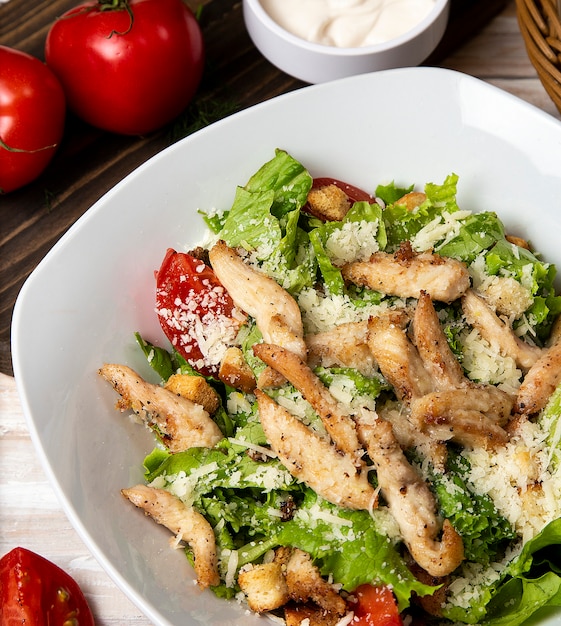 Chicken parmesan caesar salad with lettuce, cherry tomatoes inside a white bowl, served with sauce and bread.