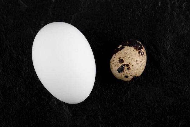Куриные и перепелиные яйца на черной поверхности.
