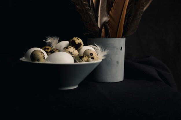 Chicken and quail eggs between feathers in bowl near big quills in old can