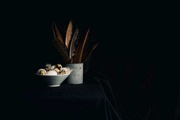 Chicken and quail eggs between feathers in bowl near quills in old can