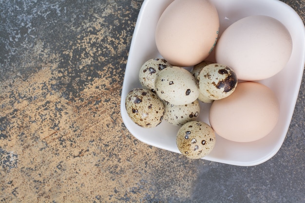 Free photo chicken and quail eggs on white bowl.