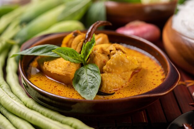 Chicken red curry in a bowl with dried chilies, basil, cucumber and long beans