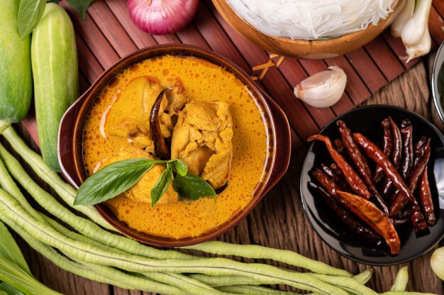 Chicken red curry in a bowl with dried chilies, basil, cucumber and long beans