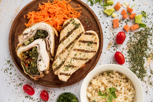 Chicken roll and breast on wooden plate arranged with vegetable pieces 