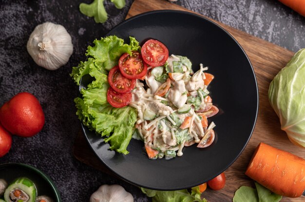 Chicken salad with tomato, needle mushroom, carrots, lettuce and cucumber on a black plate