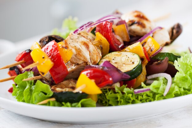 Chicken skewers with onions on top of a salad