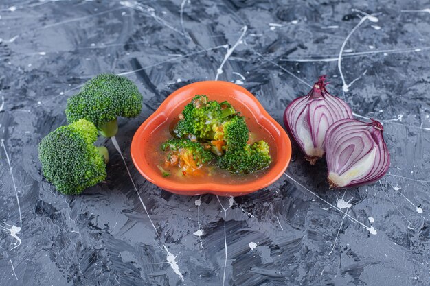 Куриный суп, брокколи и лук на синей поверхности