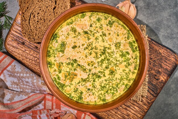 Chicken soup with vegetables and mushrooms, top view, close-up. Served with black bread and garlic. A healthy hot winter lunch. Layout on gray background