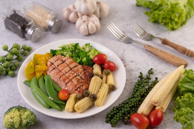 Куриный стейк с белым кунжутом, горошком, помидорами, брокколи и тыквой на белой тарелке.