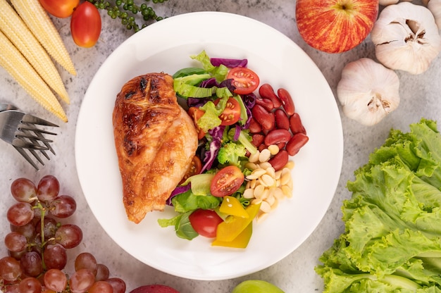 Chicken steak topped with white sesame, peas, tomatoes, broccoli and pumpkin in a white plate.