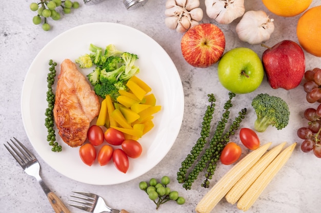 Chicken steak topped with white sesame, peas, tomatoes, broccoli and pumpkin in a white plate.