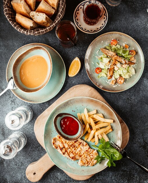 Куриный стейк с картофелем фри и кетчупом, подается с супом и салатом Цезарь