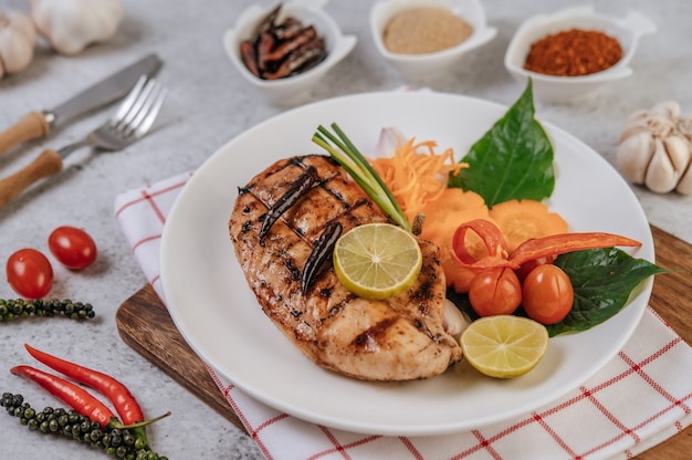 Bistecca di pollo con limone, pomodoro, peperoncino e carota sul piatto bianco.