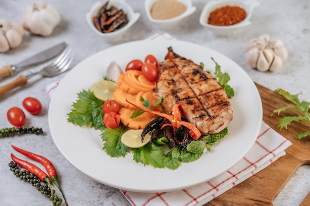 Foto gratuita bistecca di pollo con limone, pomodoro, peperoncino e carota sul piatto bianco.