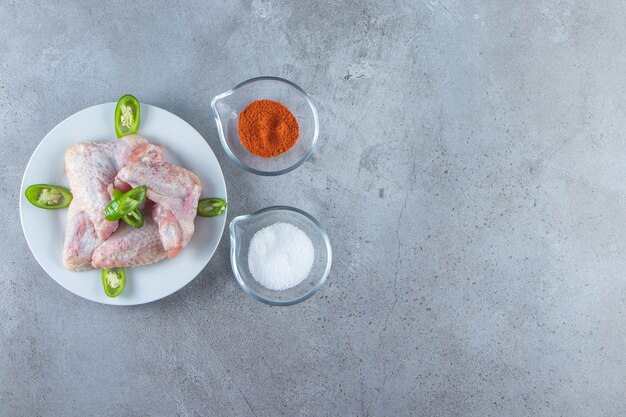 Chicken wings on a plate next to spice and salt bowls, on the marble background. 