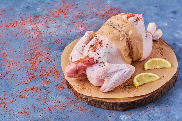 Chicken with lemon and spices on a wooden board on blue
