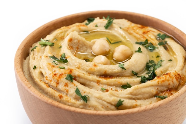 Chickpea hummus in a wooden bowl garnished with parsley paprika and olive oil isolated on white background