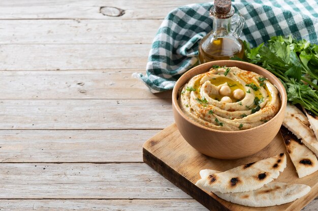 Chickpea hummus in a wooden bowl garnished with parsley paprika and olive oil on wooden table