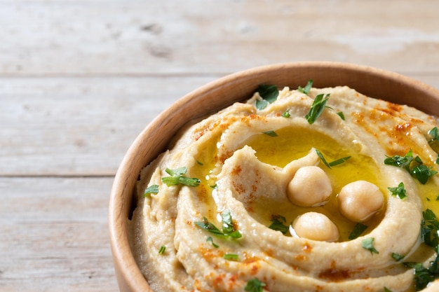 Chickpea hummus in a wooden bowl garnished with parsley paprika and olive oil on wooden table