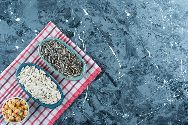 Chickpea and sunflower seeds on bowls on the tea towel, on the blue table. 