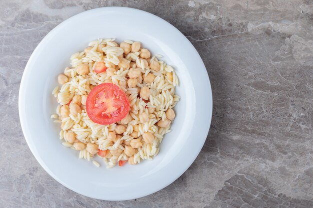Chickpeas and pasta with slice tomato on the plate , on the marble.