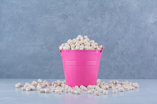 Chickpeas in and scattered around a small purple bucket on marble background.