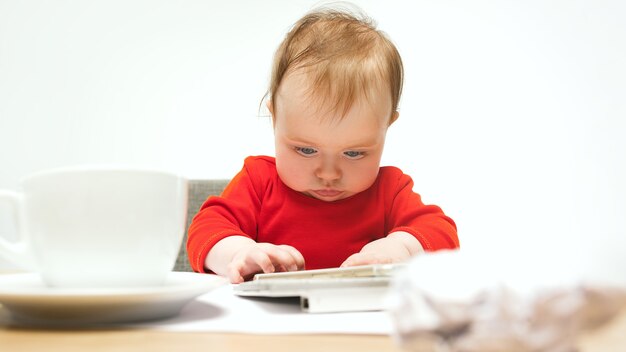 Child baby girl sitting with keyboard of modern computer or laptop in white studio.