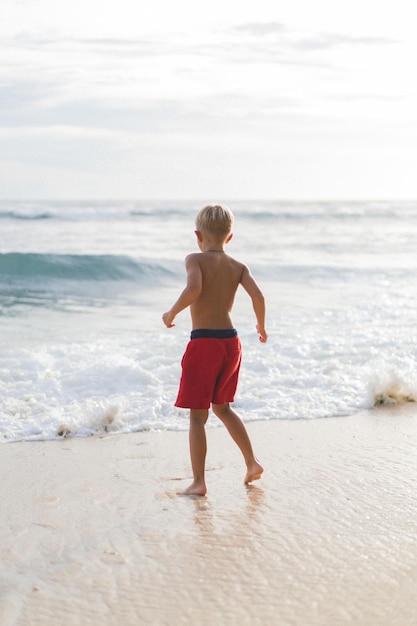 해변의 아이가 바다의 파도에서 놀고 있습니다. 바다의 소년, 행복한 어린 시절. 열대 생활.