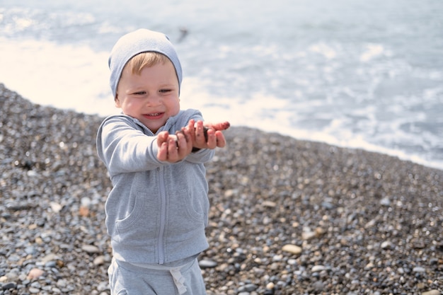 Child blond boy playing with rocks and sand on the beach on a sunny day in spring or autumn
