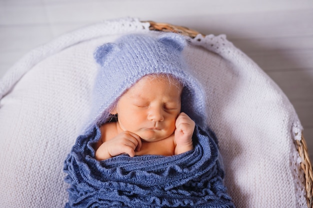 Il bambino in cappello blu e sciarpa lavorata a maglia dorme sul cuscino bianco nel canestro