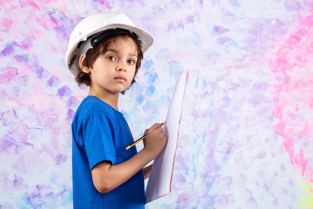 child boy in blue t-shirt writing paper plan in blue t-shirt and white helmet on colored