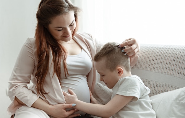 自宅のソファで妊娠中の母親の腹を抱き締める少年。