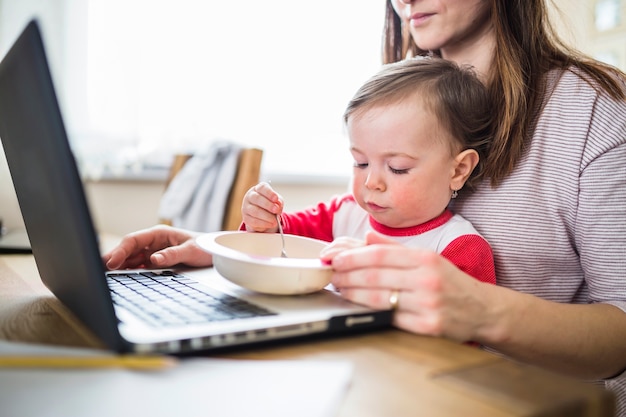 ラップトップで働いている母親の食べ物を食べる子供