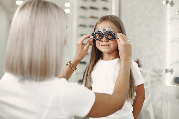 Проверка зрения у ребенка и проверка зрения. Маленькая девочка, проверяющая глаза, с фороптером. Врач выполняет проверку зрения для ребенка