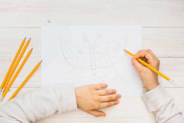 Child hand sketching butterfly with pencil on wooden background