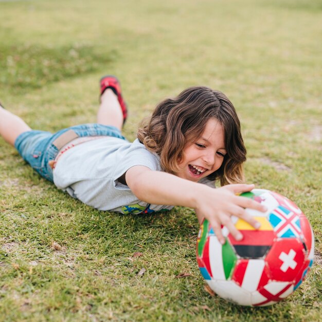 Child lying in grass and playing with ball