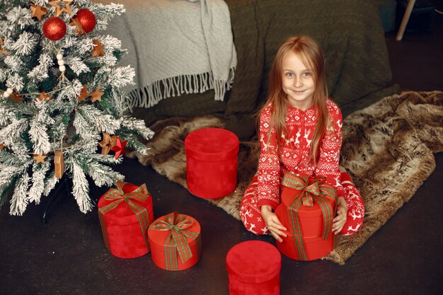 Child in a red pajamas. Daughter sitting near Christmas tree.