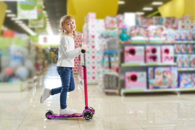 Child riding scooter in big store with toys.