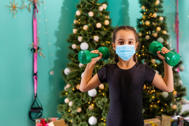 Child in a Santa hat wearing medical face mask with Christmas gift box. Christmas shopping. Copy space.