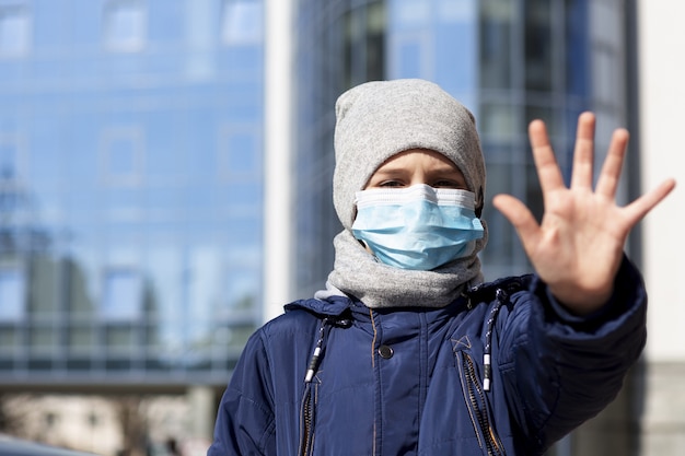 Bambino che mostra mano mentre indossa la maschera medica fuori