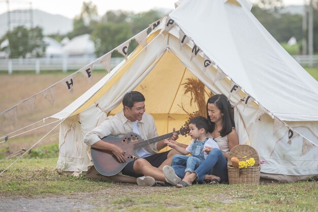 캠핑에 웃는 가족과 함께 노래하는 아이. 시골에서 캠핑 휴가 즐기는 가족.