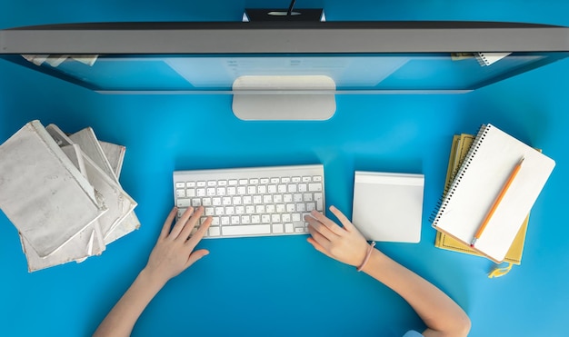 A child sits in front of a computer with notepads and books top view